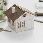 Model of a home next to a key and money